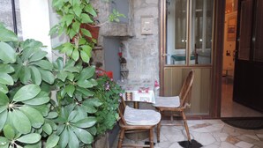 A corner of a room with a stone wall, a wooden chair, a table with a patterned tablecloth, and a potted plant with green leaves. - Apartment Pera (Split)