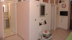 A room with a glass-top table, a clock on the wall, and a door leading to another room. - Apartment Pera (Split)