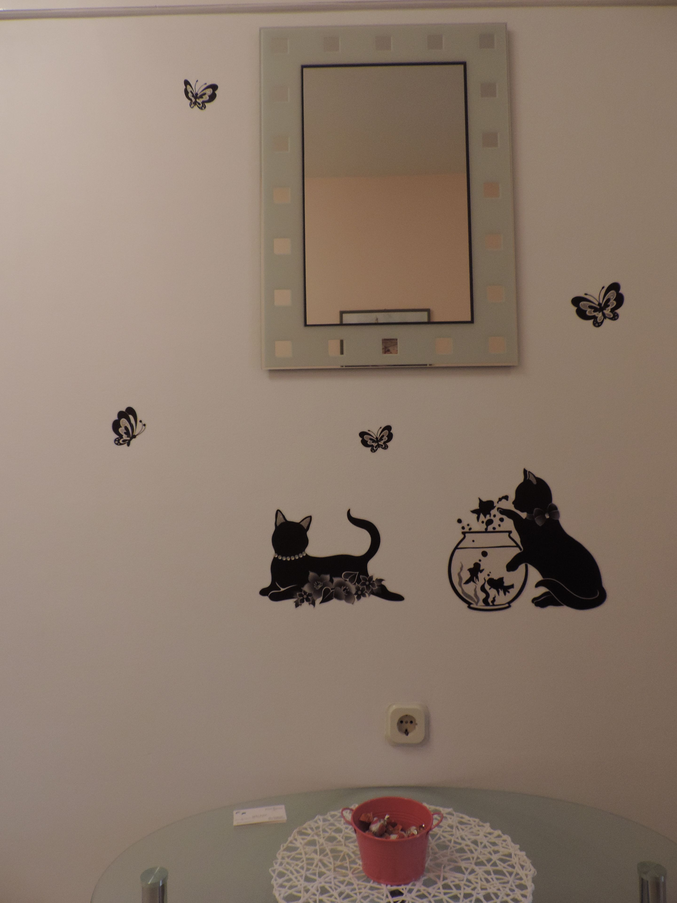 A wall with a large mirror, decorative butterfly stickers, and two cat stickers.