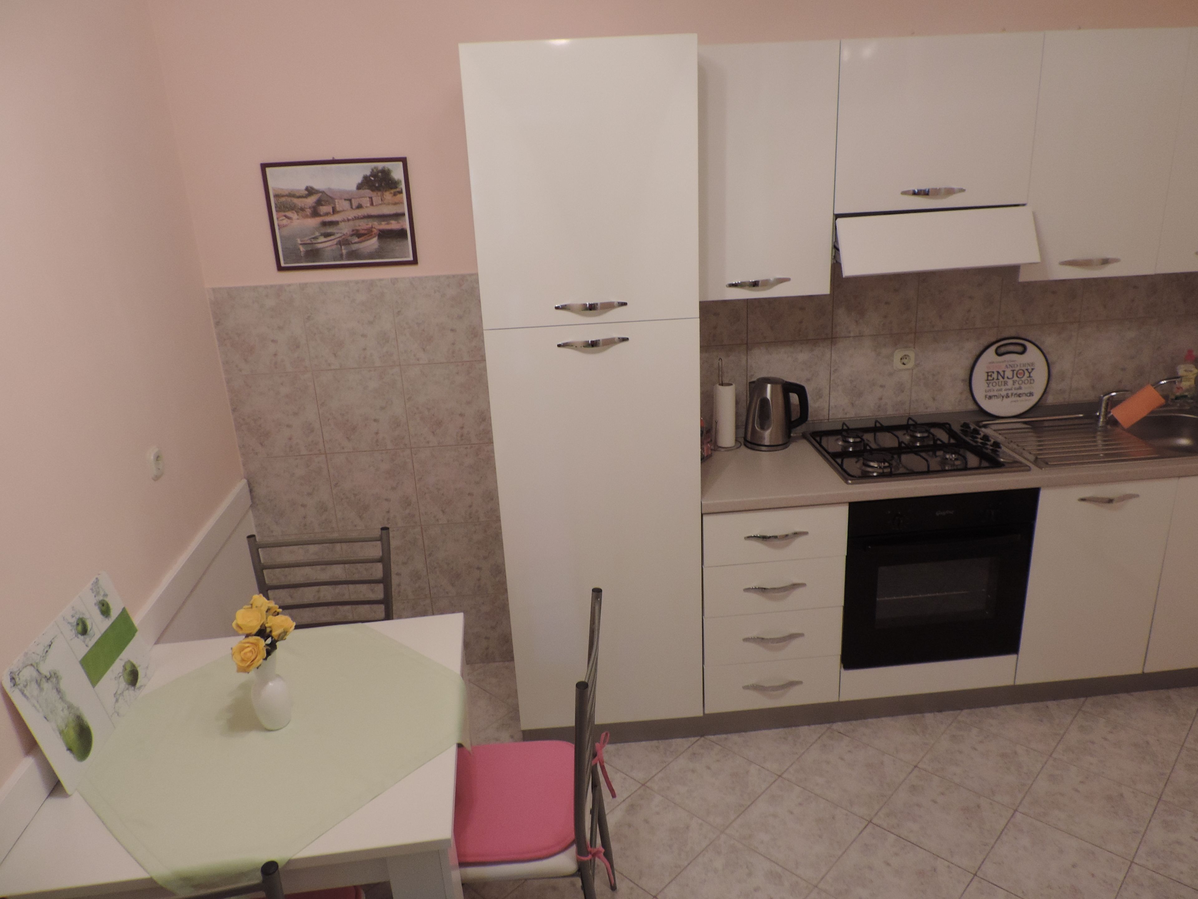 A compact kitchen with white cabinets, a gas stove, a sink, and a dining table with a vase of yellow flowers.