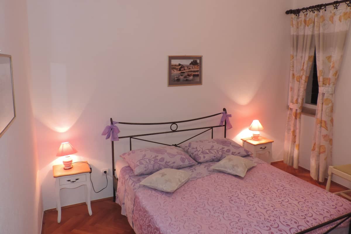 A bedroom with a bed, two bedside tables with lamps, a picture on the wall, and a window with curtains.