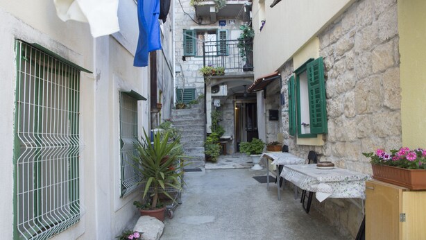 A narrow courtyard with a stone building, a table with a tablecloth, and potted plants. - Apartment Pera (Split)