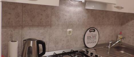 A kitchen with white cabinets, a gas stove, a kettle, and a sink.