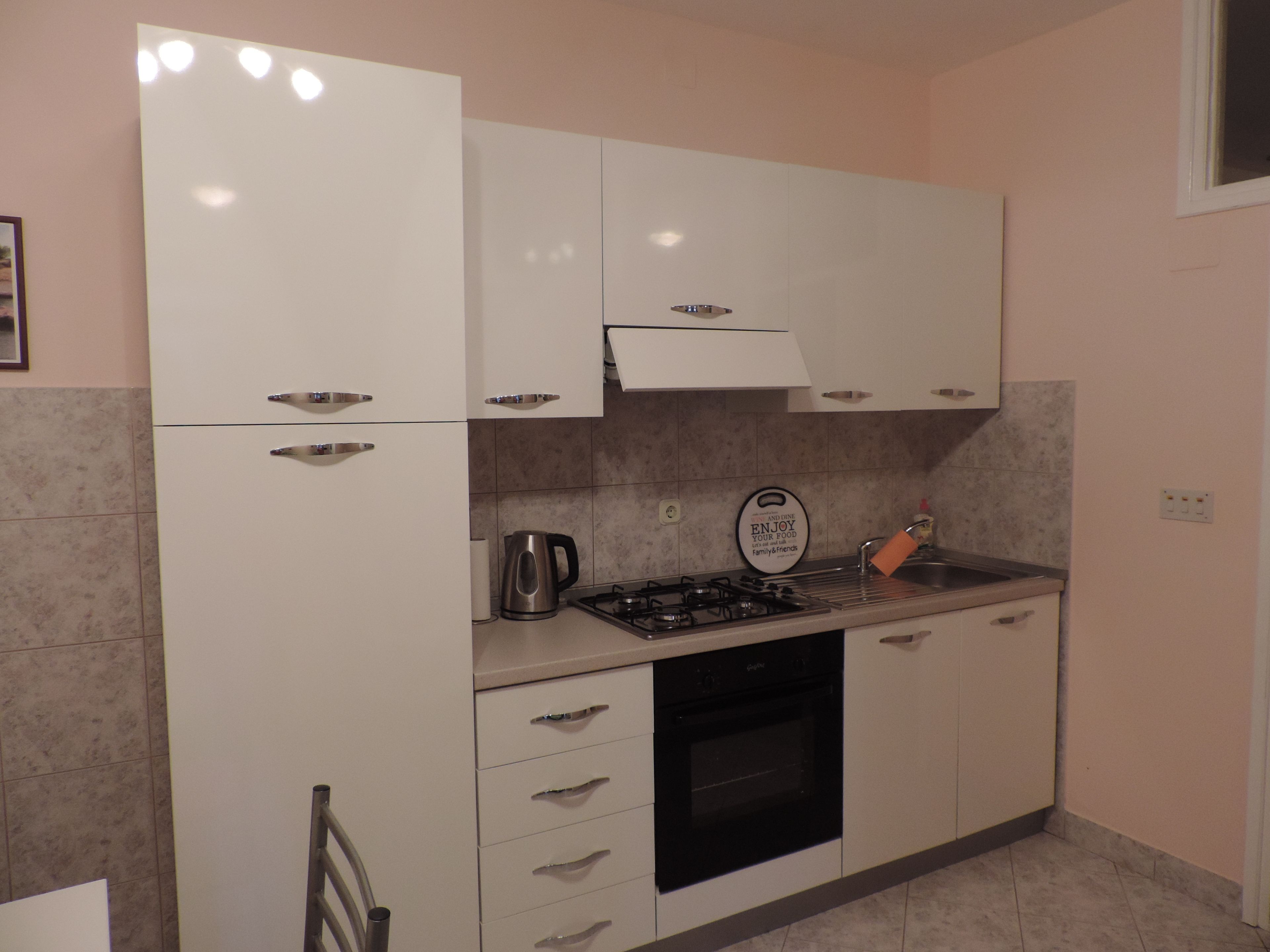 A compact kitchen with white cabinets, a gas stove, a kettle, and a toaster.