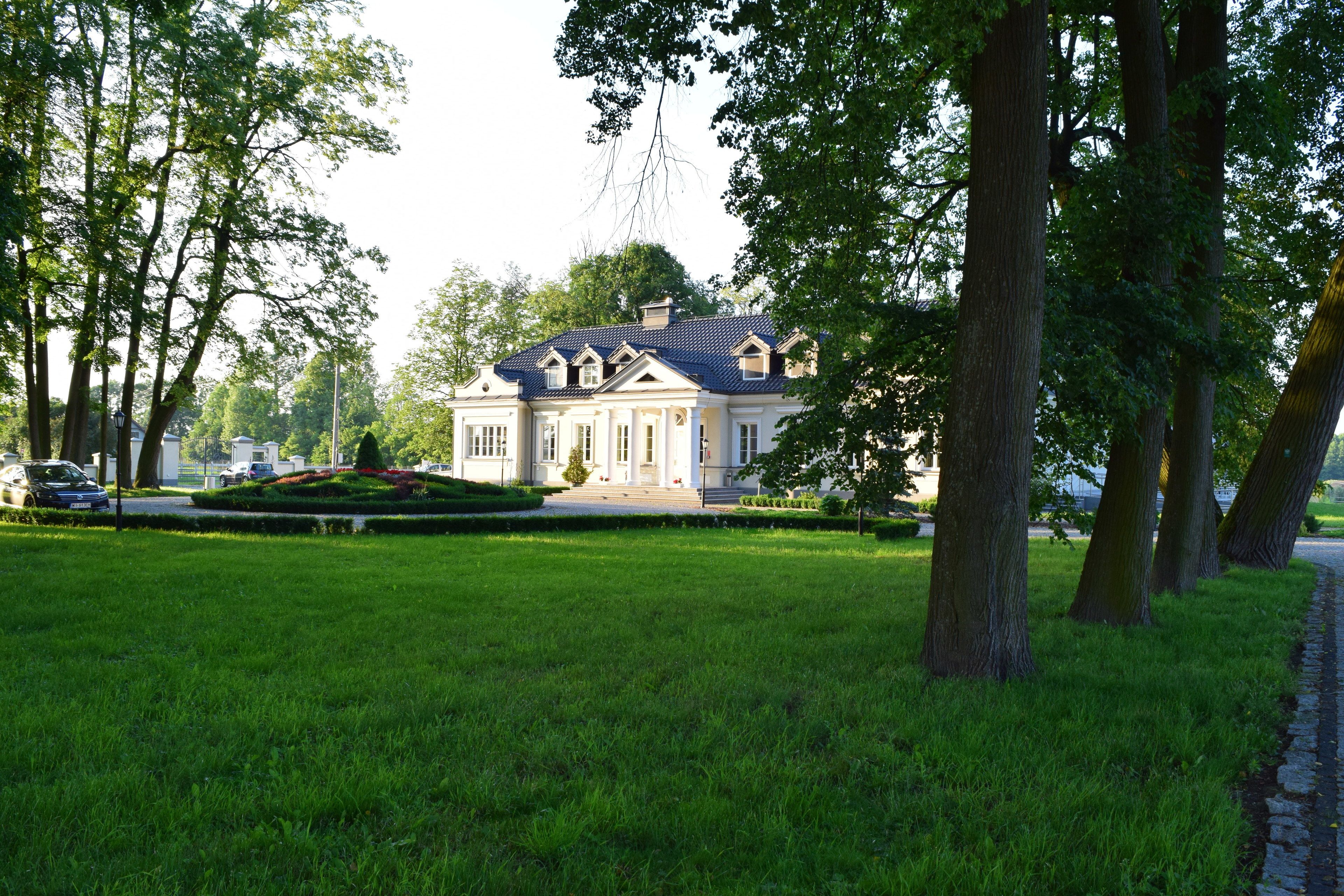 Een groot, statig gebouw met een symmetrische gevel, een verzorgd gazon en een verharde oprit naar de ingang.