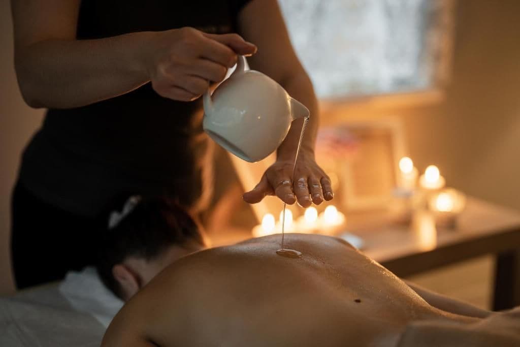 A person receiving a treatment with a white container being poured onto their back.