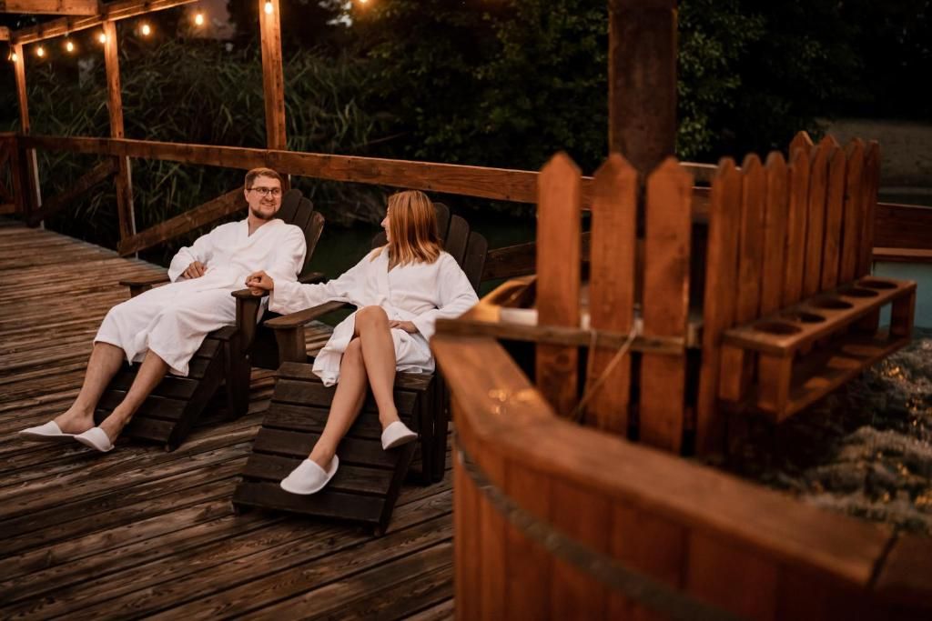 Two individuals seated on wooden loungers on a wooden deck with string lights overhead.