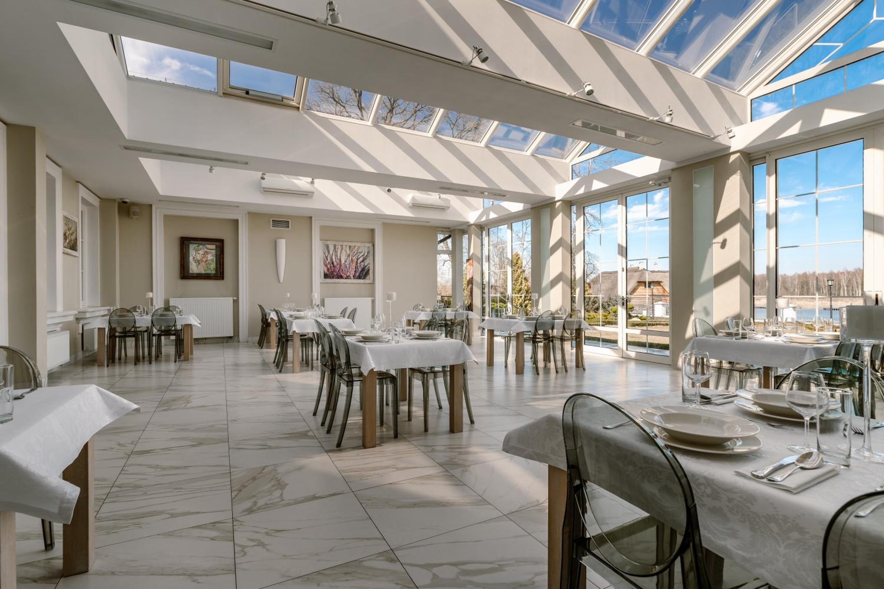 A spacious dining area with multiple tables and chairs, large windows, and a high ceiling with skylights.