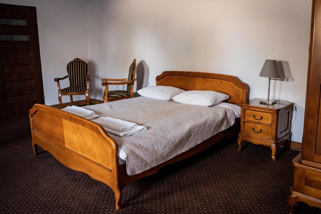 A wooden bed with a headboard, a nightstand with a lamp, a chair, and a door.
