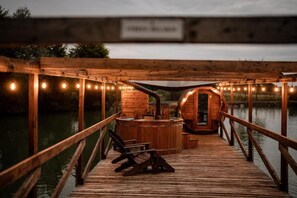A wooden deck with a hot tub and seating area, surrounded by a wooden railing and string lights. - Hotel Przy Dworze (Lesna Podlaska)