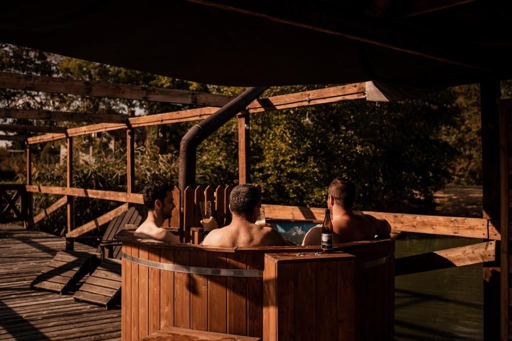 Uma banheira de hidromassagem de madeira com duas pessoas dentro, cercada por um deck de madeira e um cercado de madeira.