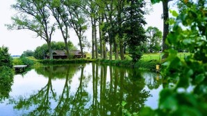 A tranquil riverside scene with a wooden bridge, a small building, and lush greenery. - Hotel Przy Dworze (Lesna Podlaska)