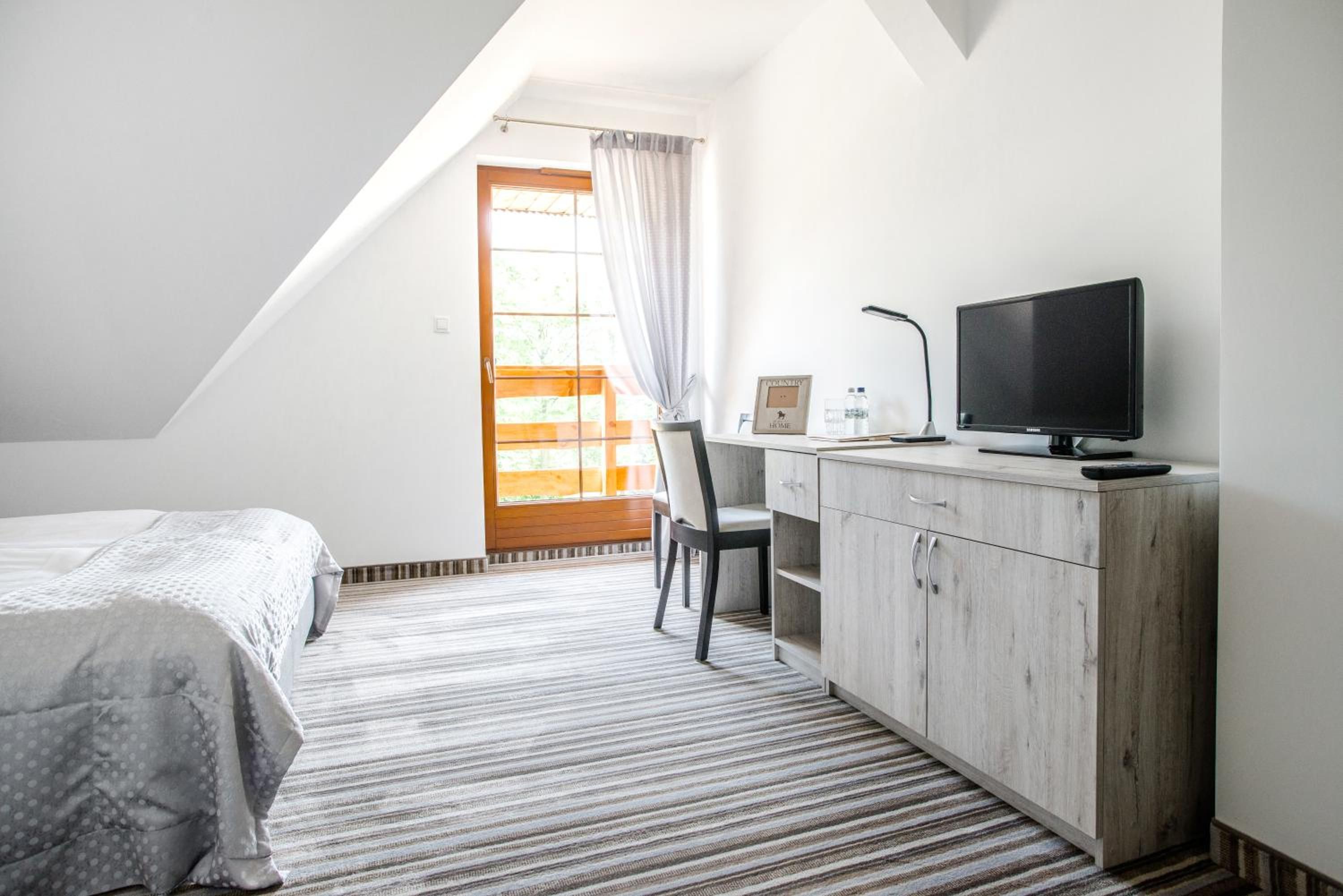 A bedroom with a bed, a desk with a TV, a chair, and a window with curtains.