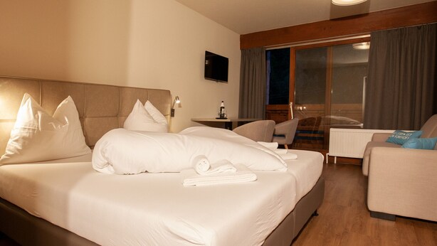 A hotel room with a large bed, a desk, a chair, and a television on the wall. - 1207 Guy´s Studio 7 (Gaschurn)