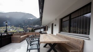 Ein moderner Außenbereich mit Essplatz, ausgestattet mit einem Holztisch, Stühlen, Bänken und Blick auf eine Berglandschaft.