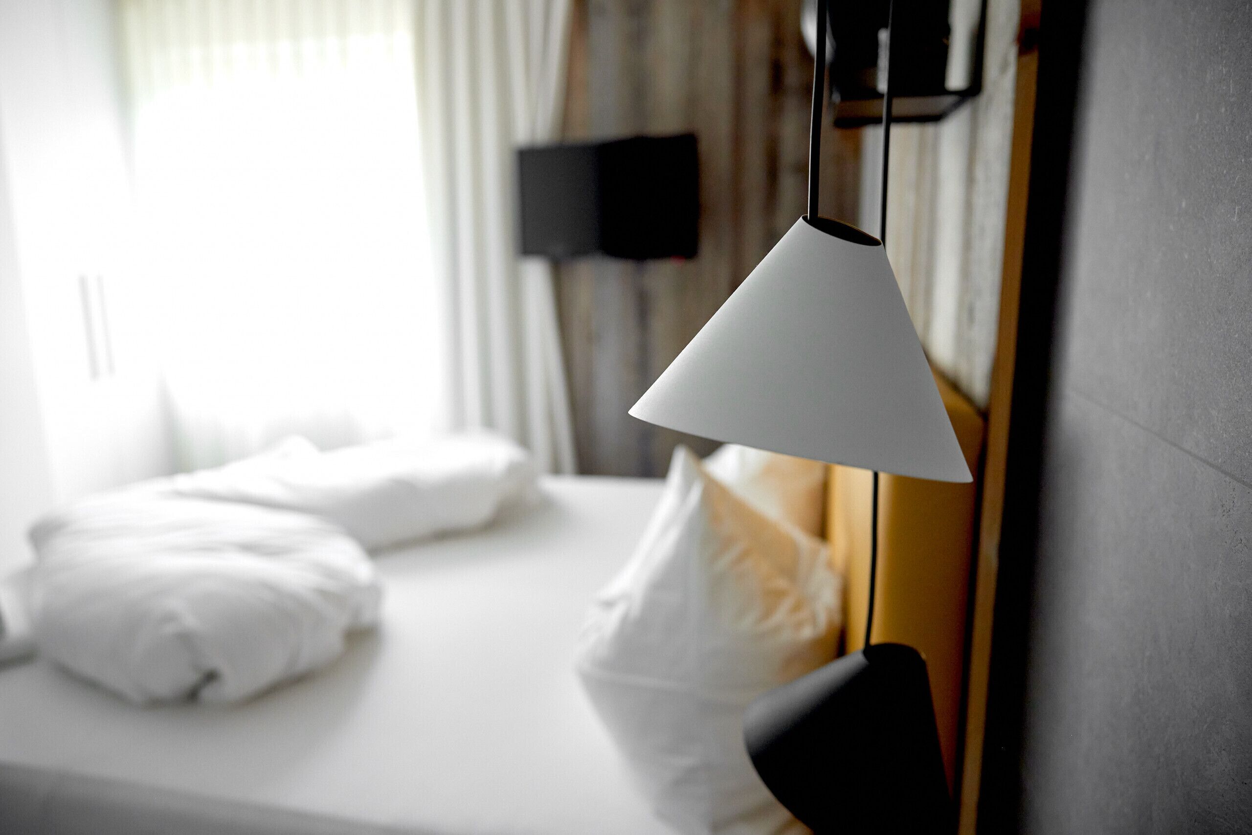 Una habitació d'hotel amb un llit ben fet, un televisor penjat i una làmpada suspesa.