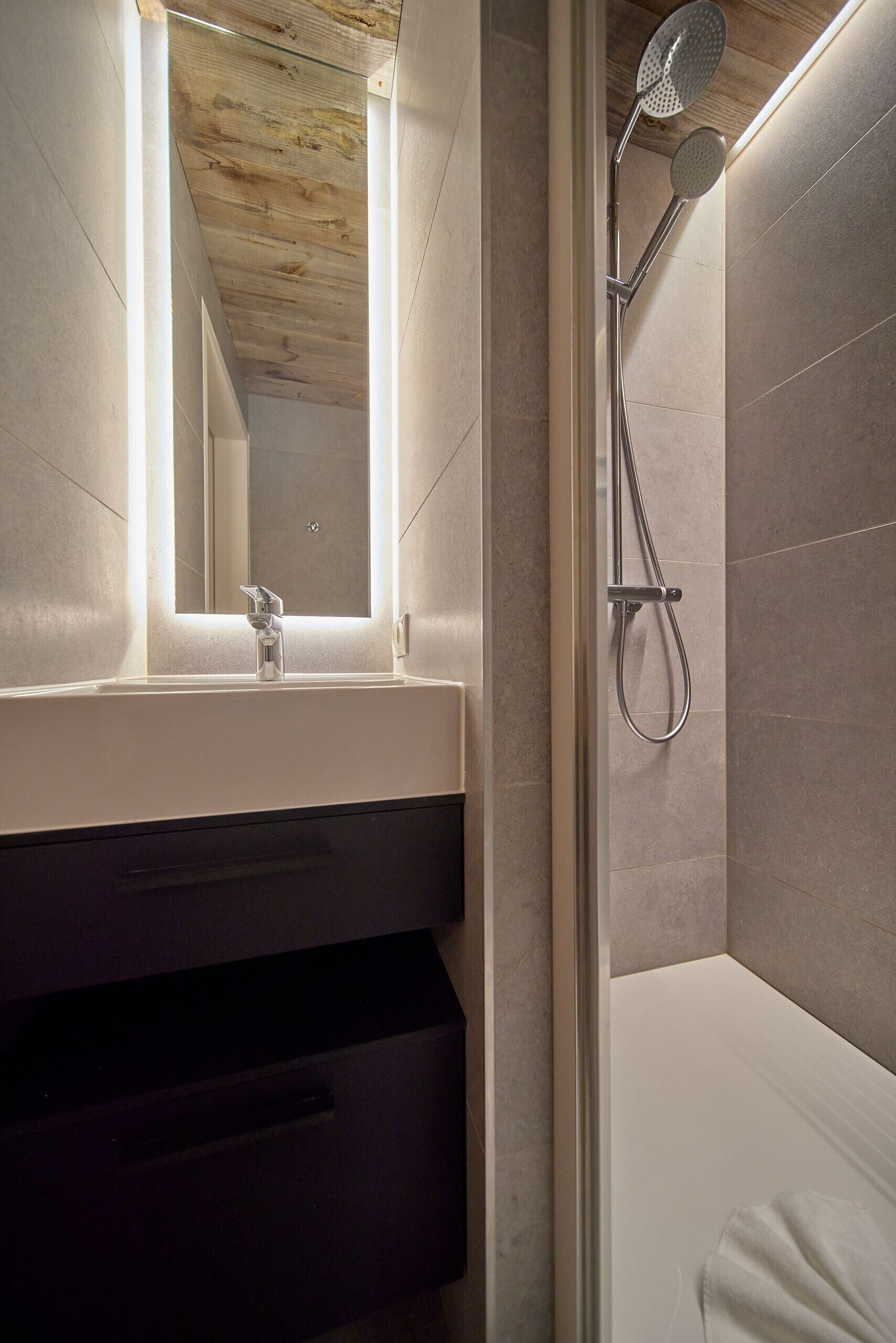 Un baño moderno con ducha, lavabo con espejo y techo de madera.