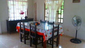 A dining area with a glass table and chairs, a fan, and a vase with flowers. - Finca Vacacional Villavicencio (Villavicencio)