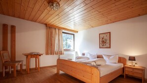 Une chambre à coucher avec un lit en bois, une table de chevet, une chaise, une table et une fenêtre avec des rideaux.