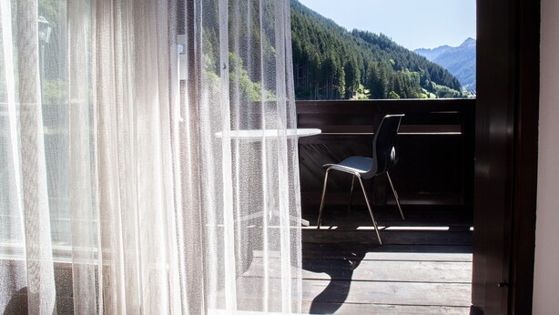 Un balcon avec une chaise et une table, donnant sur une chaîne de montagnes boisées.