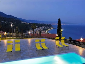 Zona junto a la piscina con tumbonas y vistas al mar.