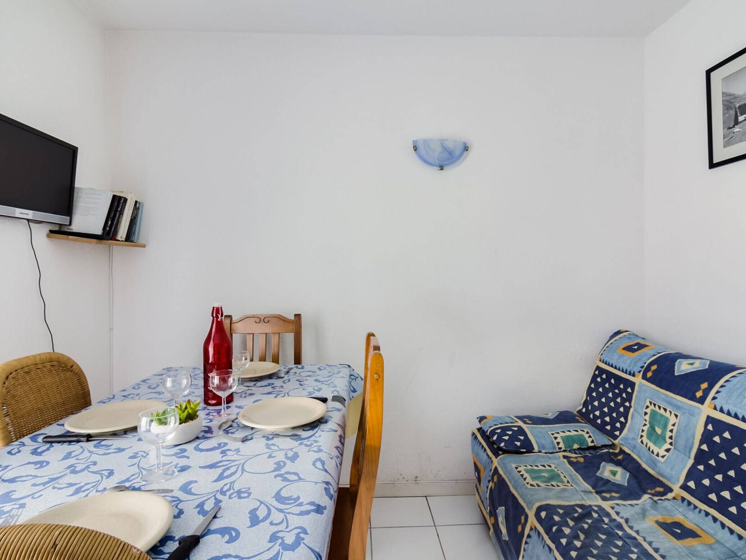 Un comedor con una mesa preparada para dos personas, una botella roja y un sofá azul con estampado.