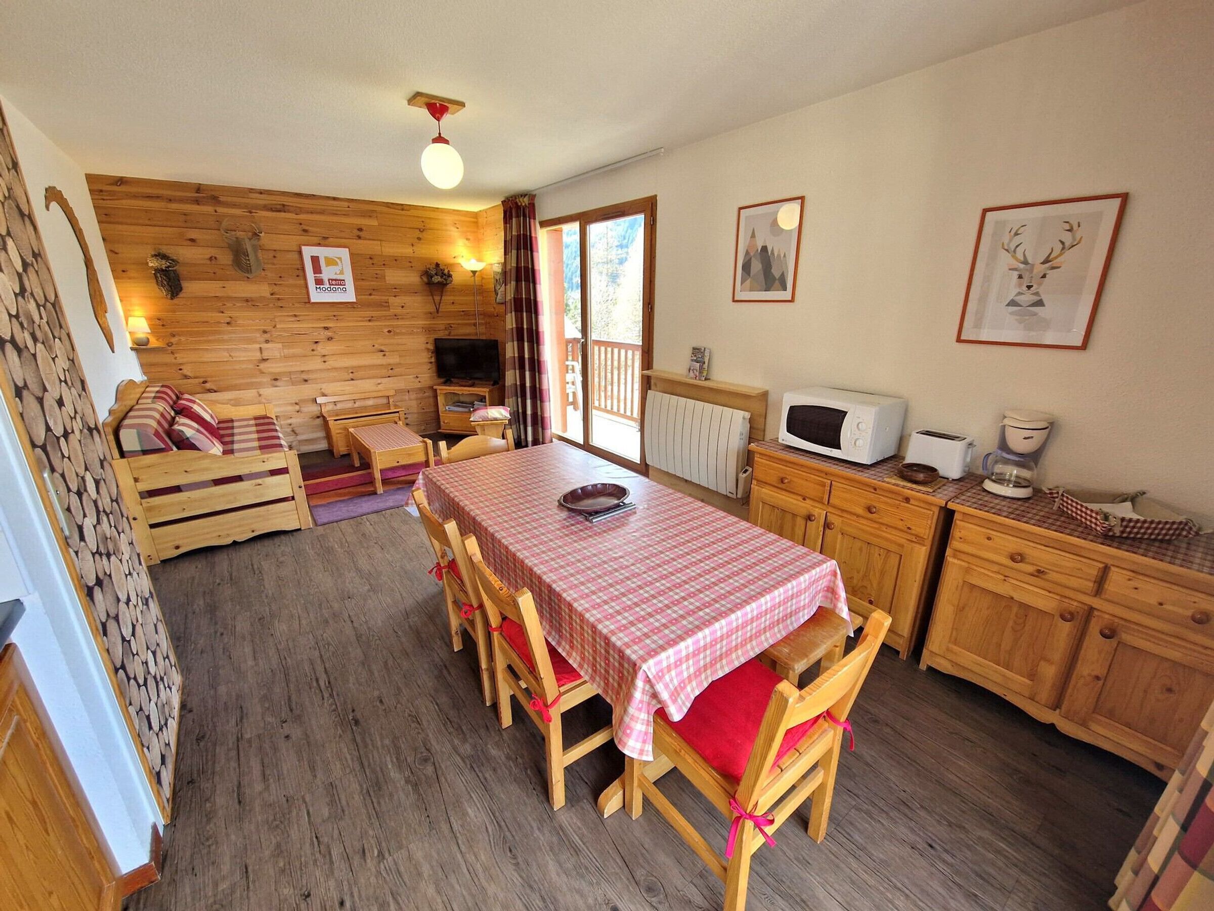 A cozy cabin-style room with a wooden interior, a dining table with chairs, a kitchenette, and a large window.