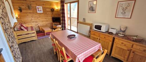 A cozy cabin-style room with a wooden interior, a dining table with chairs, a kitchenette, and a large window.