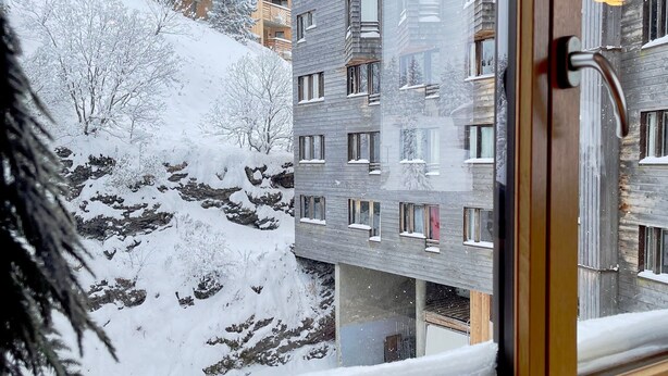 Vista desde una ventana de un edificio de varios pisos, con paisajes nevados y un picaporte visible.