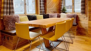 Una habitación acogedora con una mesa de madera y sillas amarillas, un sofá con cojines mullidos y ventanas amplias con cortinas.