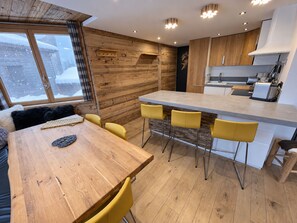 Moderni keittiö, jossa on puiset kaapit, keskellä sijaitseva saareke baarituoleineen ja ikkuna, josta avautuu lumipeitteinen maisema.
