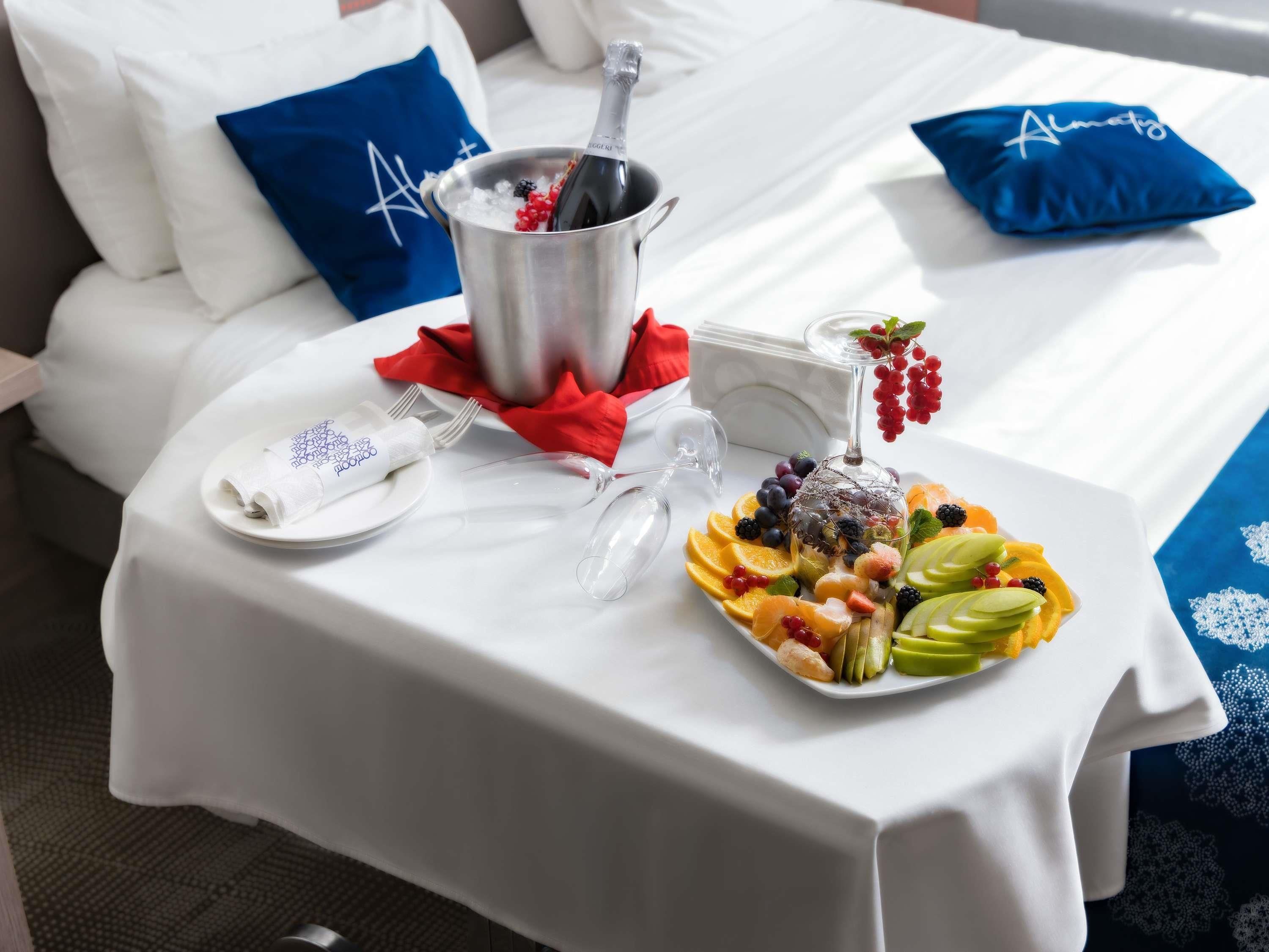 Habitación de hotel impecable con una cama, una mesita de noche con una bandeja de frutas, una botella de champán y una copa.