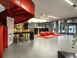 A modern hotel lobby with a red spiral staircase, a bar area, and seating. - Novotel Almaty City Center (Almaty)