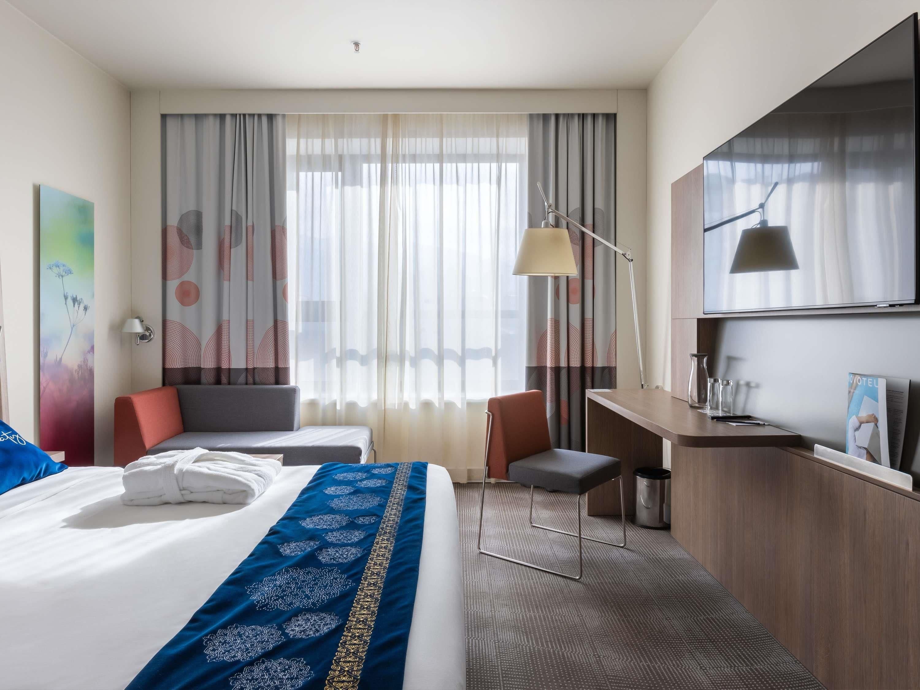 Camera d'albergo con un letto grande, una scrivania, una sedia, una TV e una finestra con tende.