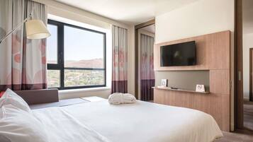 A hotel room with a large bed, a TV mounted on the wall, a window with curtains, and a view of the landscape.
