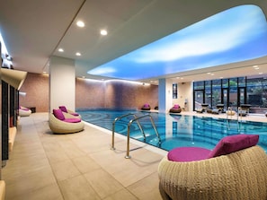 A modern indoor swimming pool with clear water, surrounded by lounge chairs and a glass wall. - Novotel Almaty City Center (Almaty)