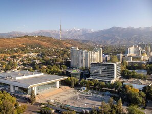 Un paisaje urbano con edificios modernos, una torre destacada y montañas al fondo.