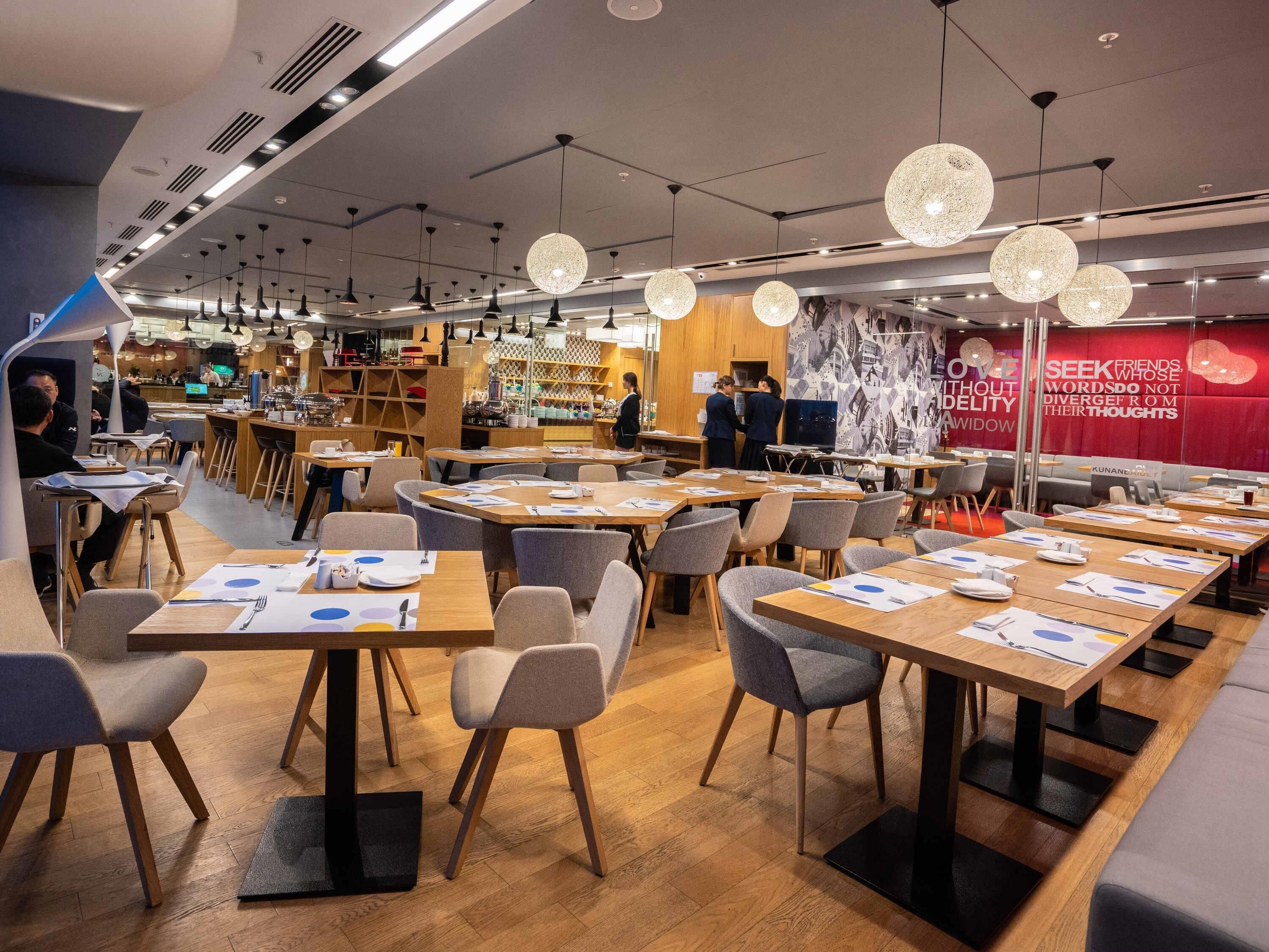 A modern restaurant with multiple dining areas, wooden tables, and hanging spherical light fixtures.