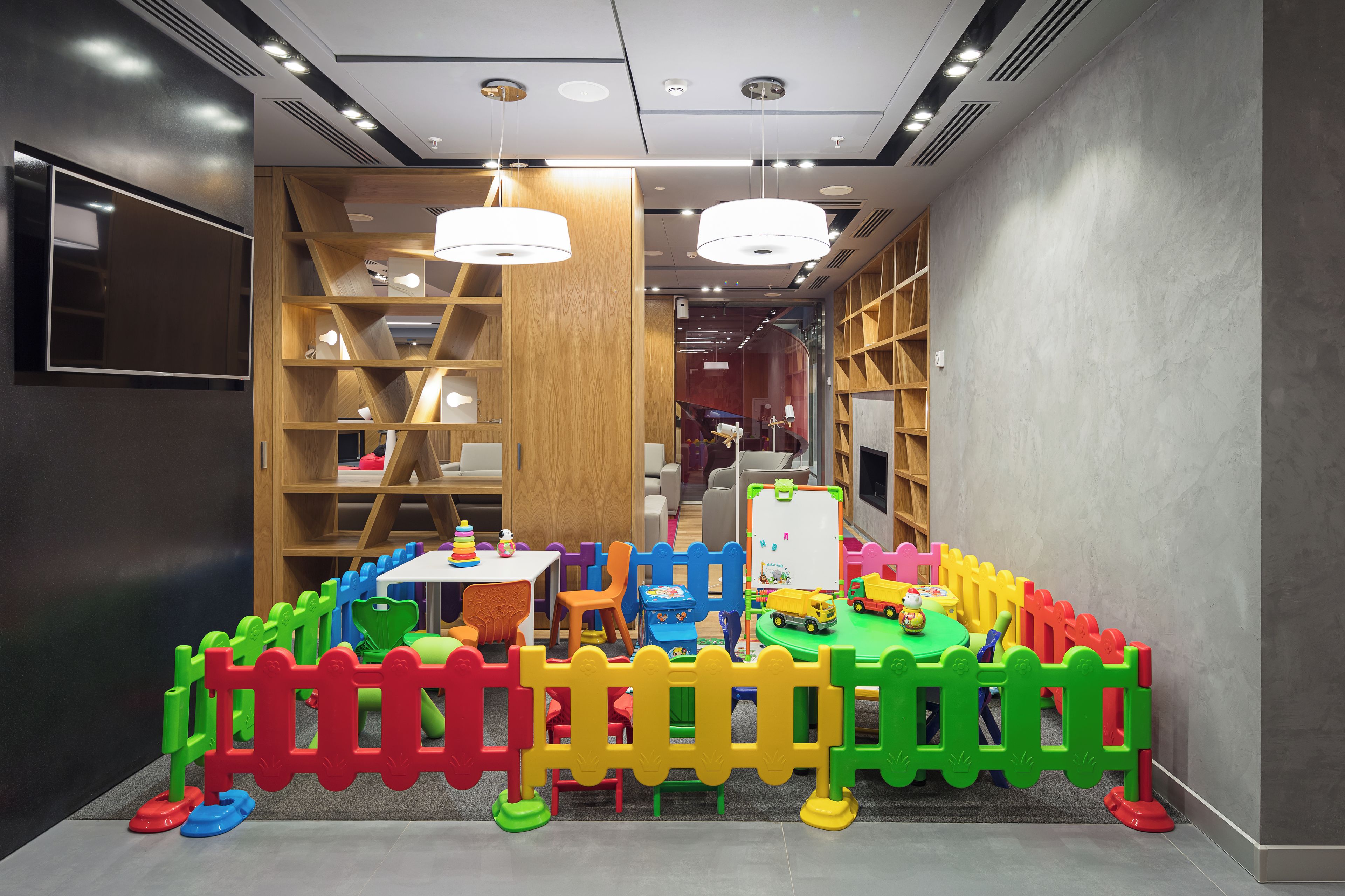 A children's play area with a colorful fence, a table with toys, and a whiteboard.