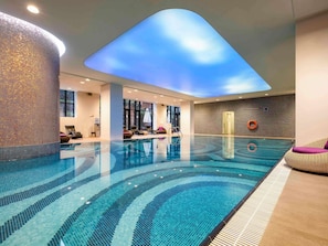 Una piscina interior con tragaluces en el techo, sillones de descanso y una pared con textura.