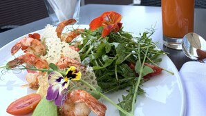 A plate of food with shrimp, greens, and a glass of orange juice on an outdoor table. - Novotel Almaty City Center (Almaty)
