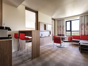 A hotel room with a bed, a TV, a desk with a chair, a sofa, and a window with a view. - Novotel Almaty City Center (Almaty)