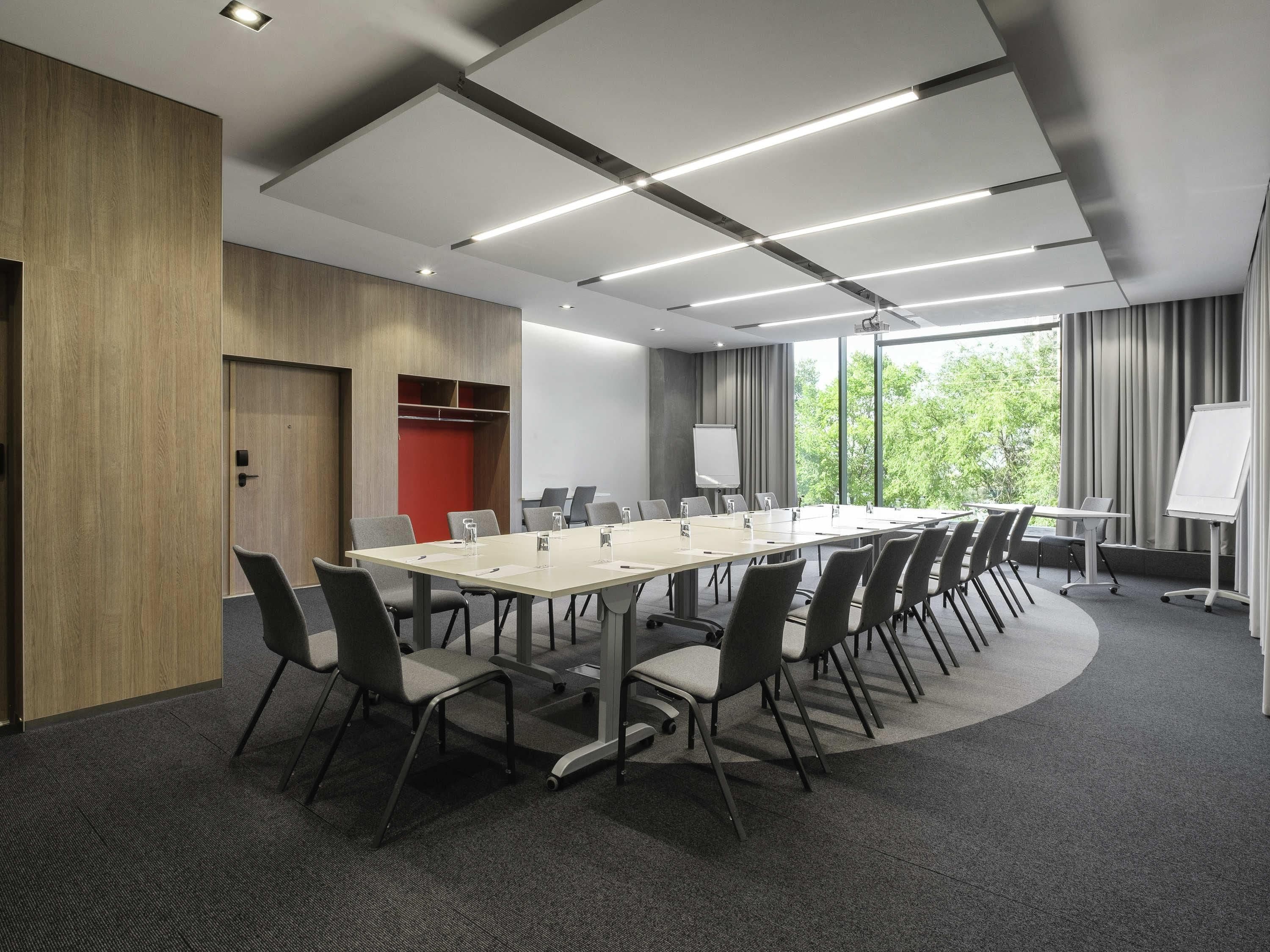 A conference room with a long table, chairs, a whiteboard, and a view of trees through large windows.