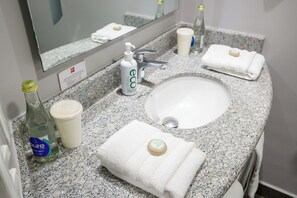 A bathroom with a granite countertop, a white sink, a mirror, a bottle of liquid soap, a cup, and a folded towel.