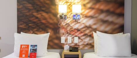 A hotel room with two beds, a nightstand with a lamp, and a large abstract painting on the wall.