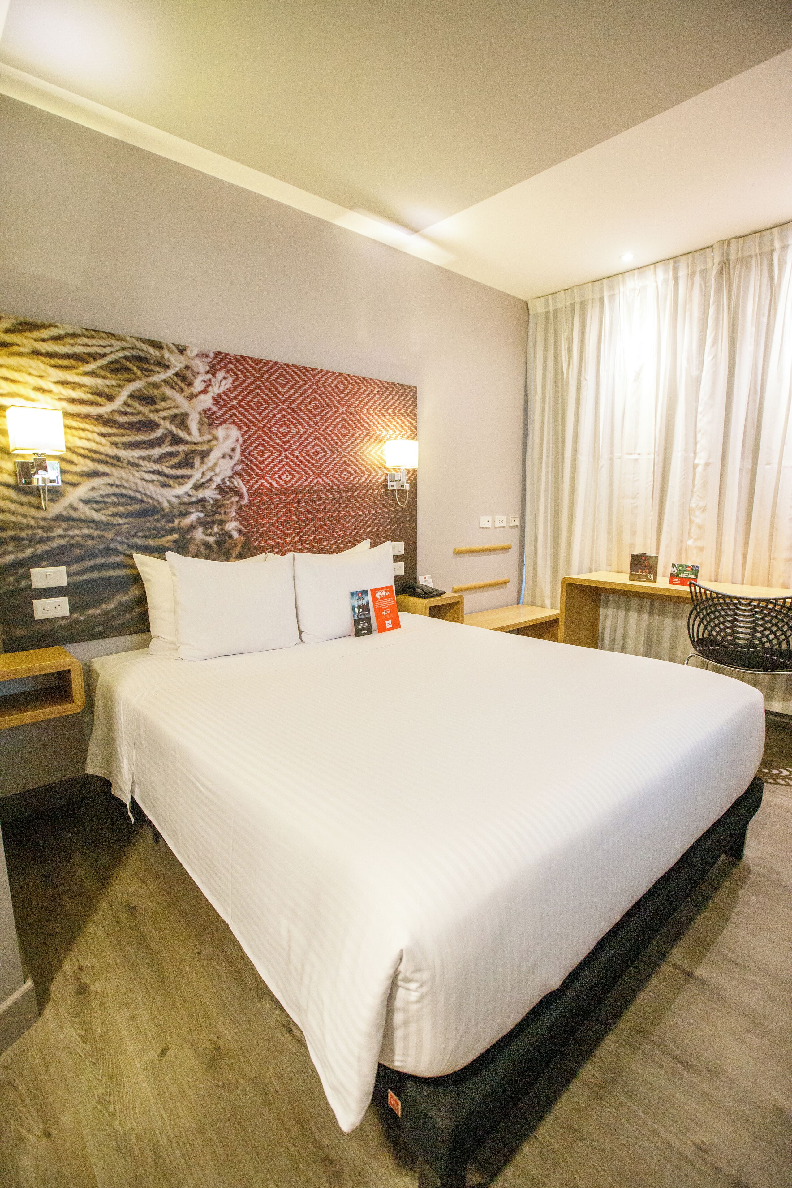 A hotel room with a large bed, a desk, a chair, and a patterned wall.
