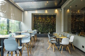 Un comedor moderno con mesas y sillas, un ventanal grande y una pared con plantas.