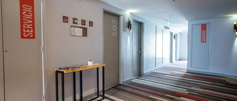 Ein Hotelkorridor mit Streifenmuster-Teppich, einem Empfangstresen und Türen mit der Aufschrift 'SERVICIO'.