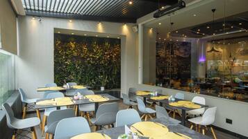Un comedor moderno con mesas dispuestas para dos, con sillas grises y manteles individuales amarillos.