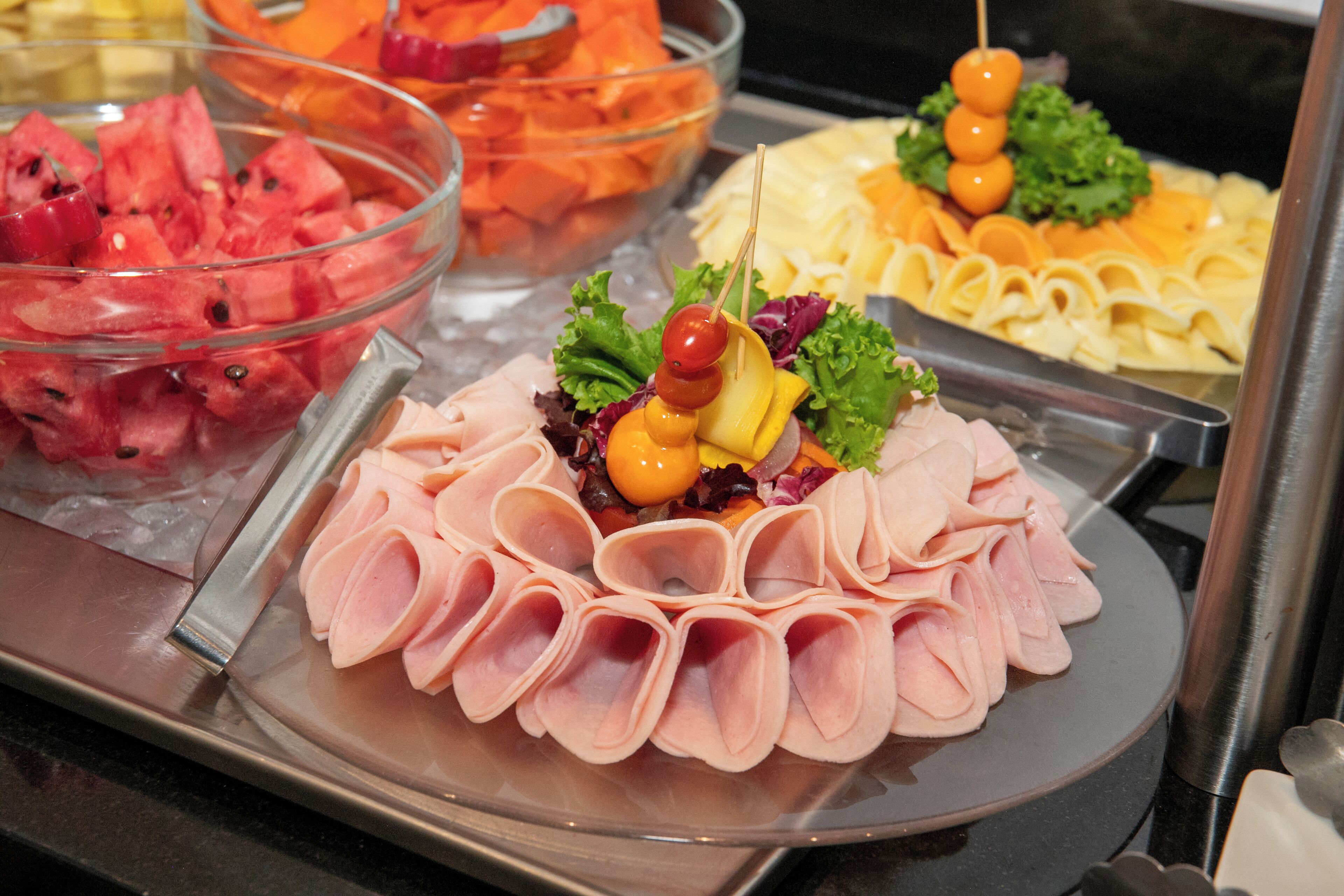 A buffet with various food items including sliced ham, watermelon, and cheese.